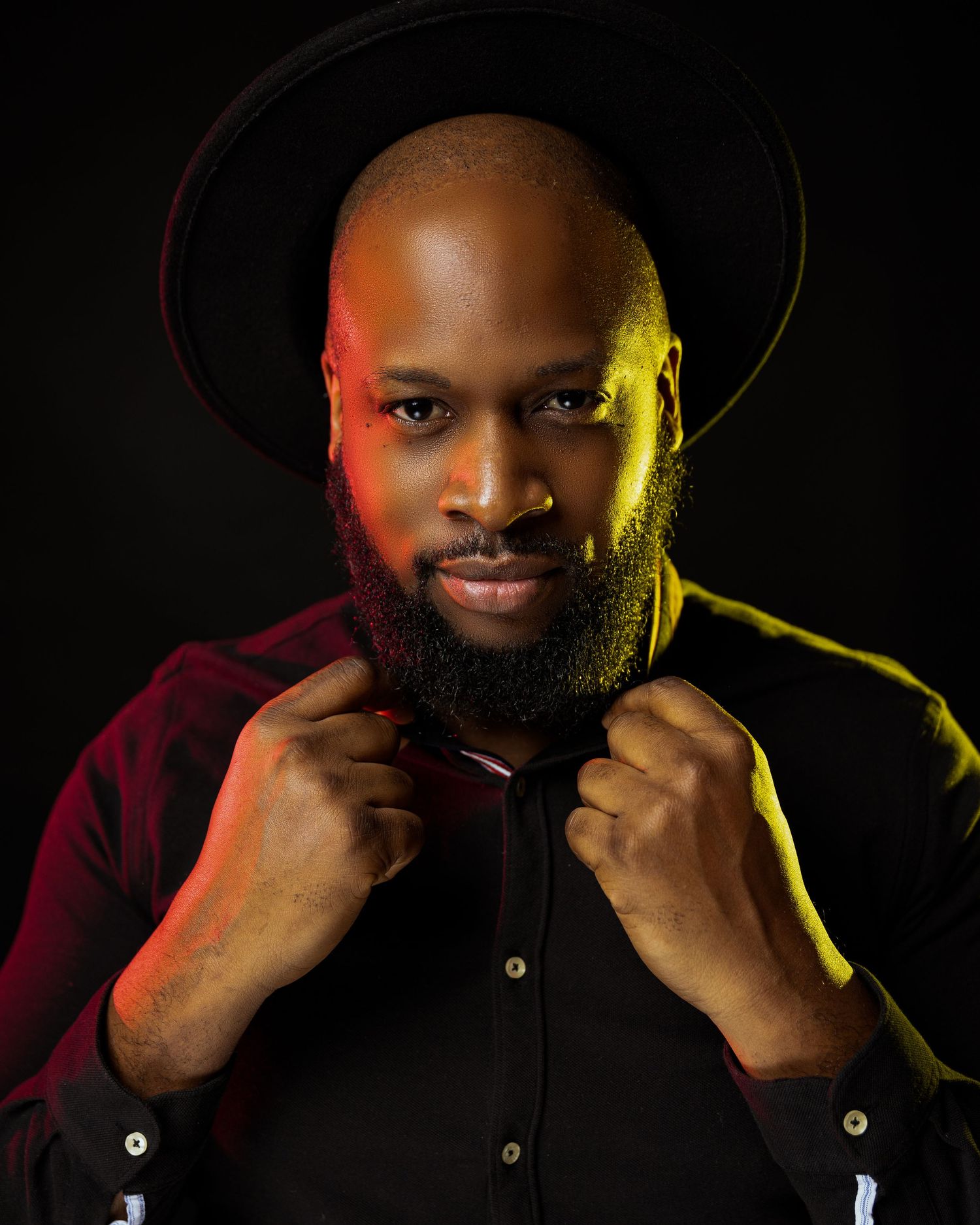 Studio portrait with dramatic red and yellow lighting against dark background highlighting beard and burgundy shirt.