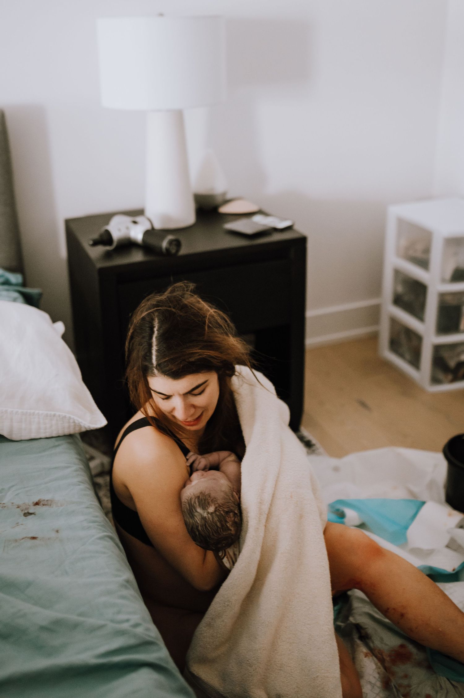 Tender moment in a bedroom with a white lamp on dark nightstand and minimal modern decor. birth photography