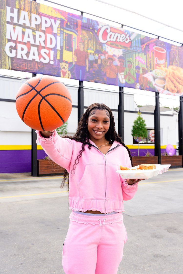 Basketball fan in pink tracksuit holding basketball outside Raising Cane's Mardi Gras celebration.