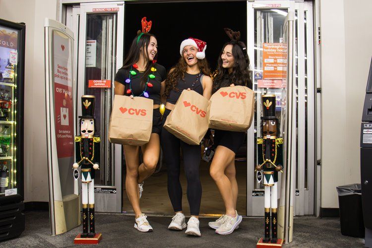 Three friends celebrating with Popeyes takeout bags while posing in doorway with holiday decorations.