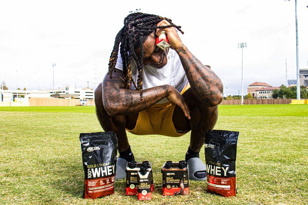Athletic figure crouching on field with protein supplement products displayed.