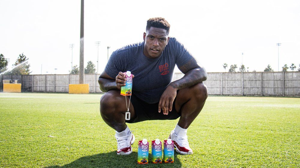 Athlete crouching on sports field with energy drinks lined up on grass.