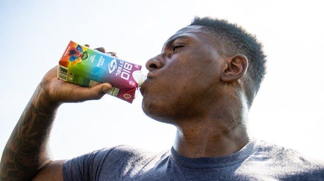 Person drinking from colorful beverage can against bright sky backdrop.