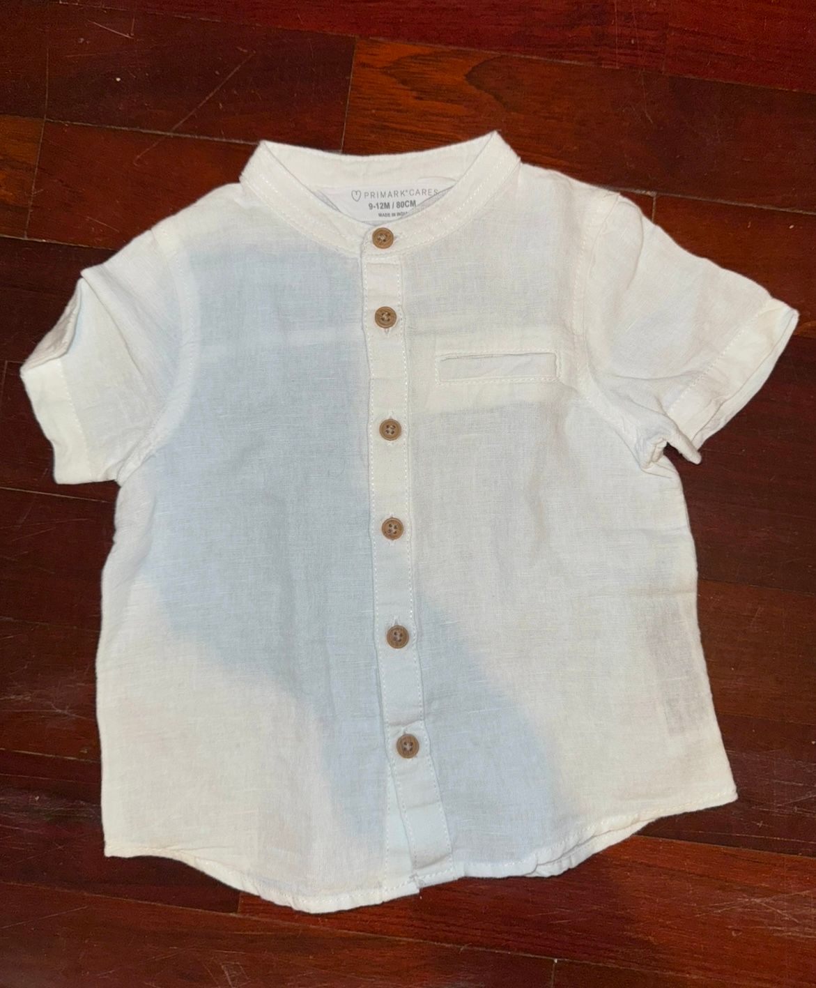 White short-sleeve button-up shirt with collar displayed on dark wood surface.