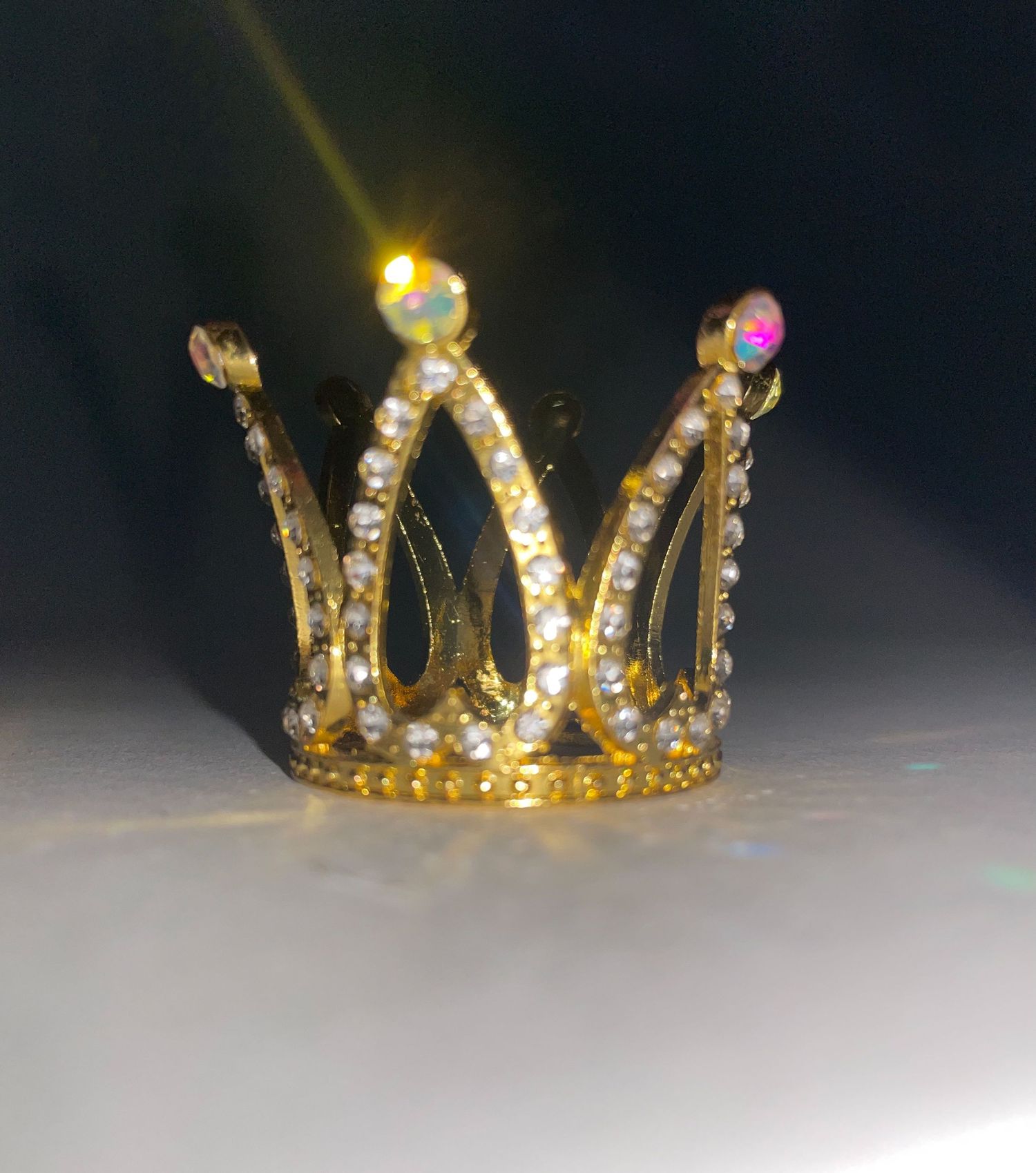 Illuminated golden crown with sparkling gems photographed against a dark background.
