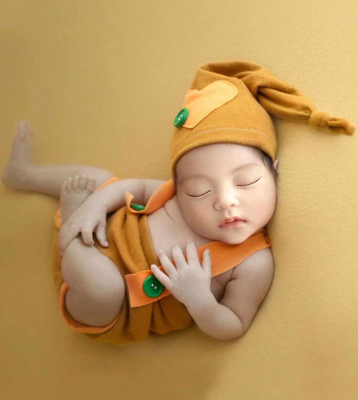 Sleeping baby wearing a cozy orange outfit on a warm yellow background.
