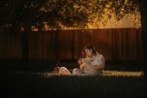 Two figures sit on grass at sunset with golden light streaming through tree branches creating a magical ambiance.