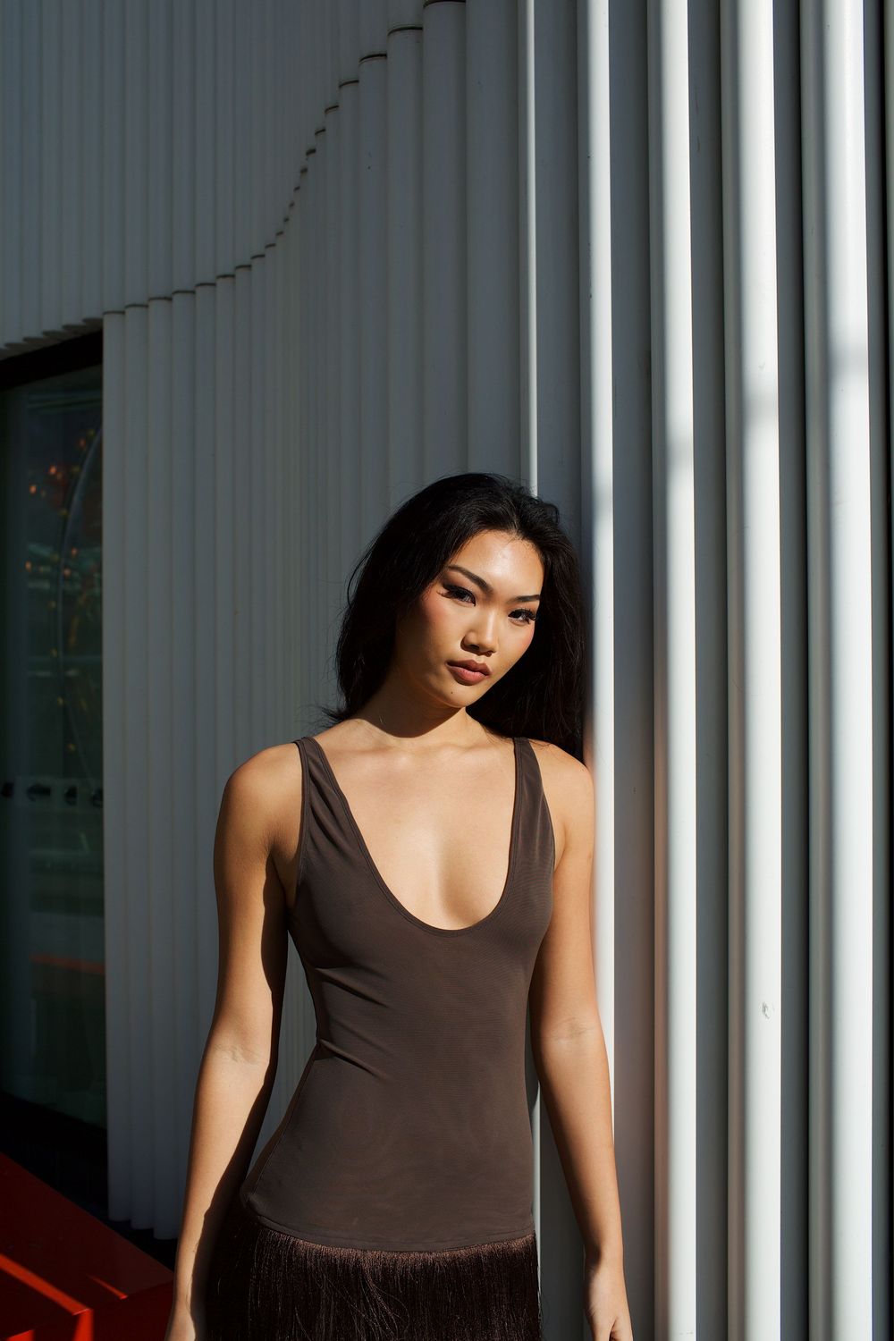 Woman in brown scoop-neck bodysuit with fringe skirt posing outdoors against white architectural columns.