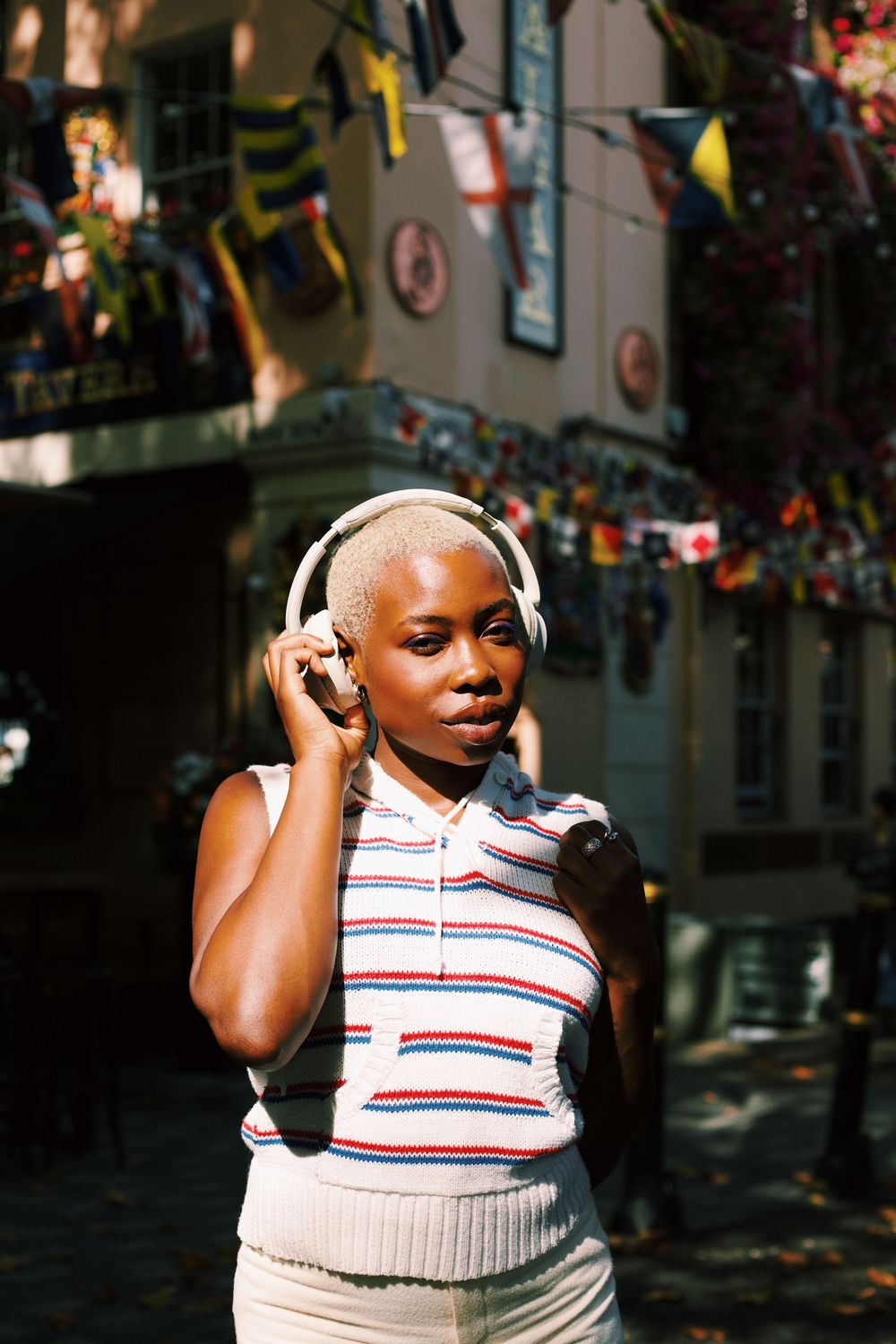 A person wearing a white and red striped polo shirt and white headphones enjoying music in an urban setting.