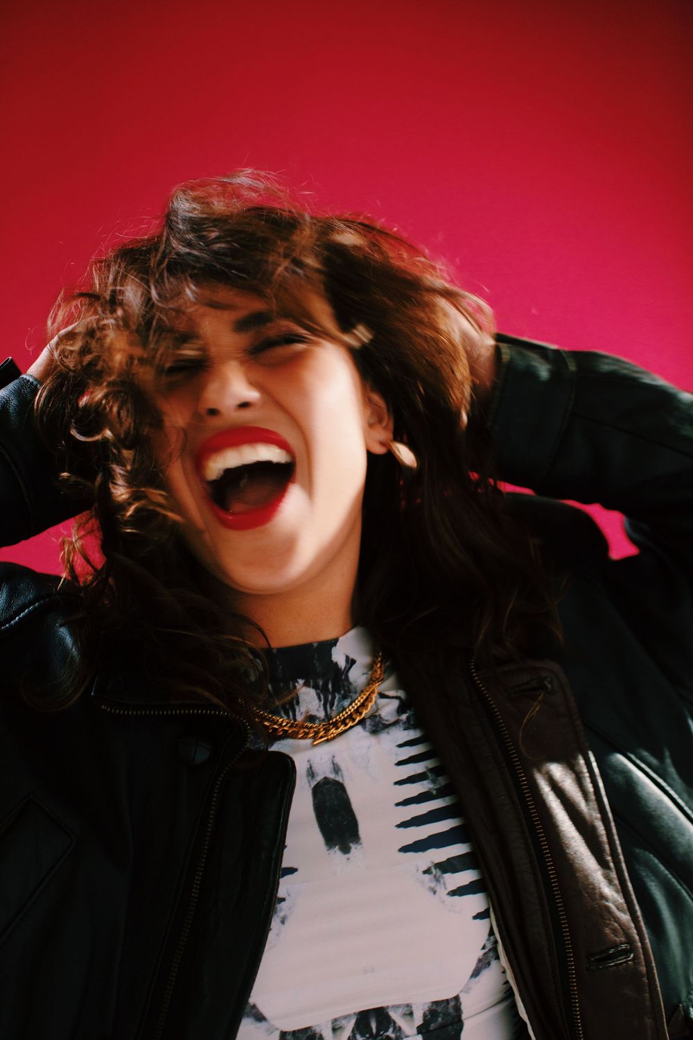 Energetic portrait against vibrant red background showing joyful expression and black leather jacket.