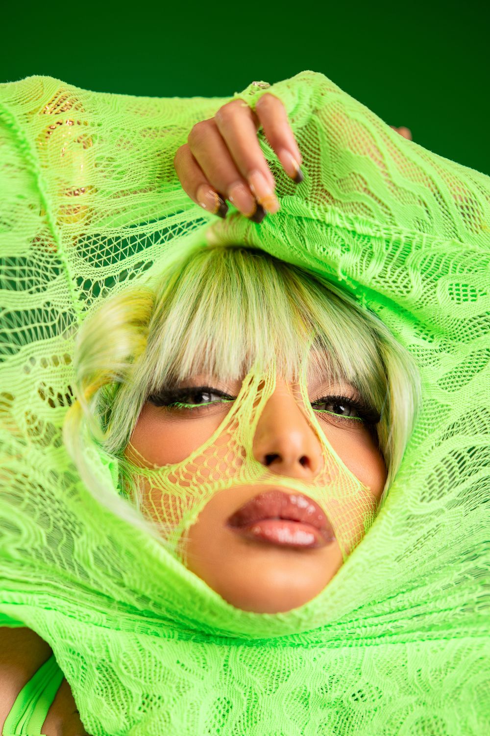 A face peeks through bright neon green lace fabric in an artistic fashion portrait series.
