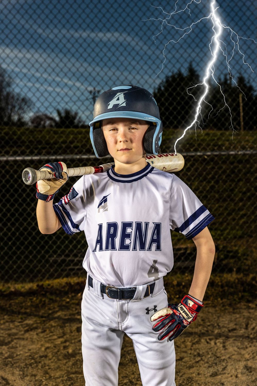 Youth baseball player in Arena uniform poses with bat against stormy sky.
