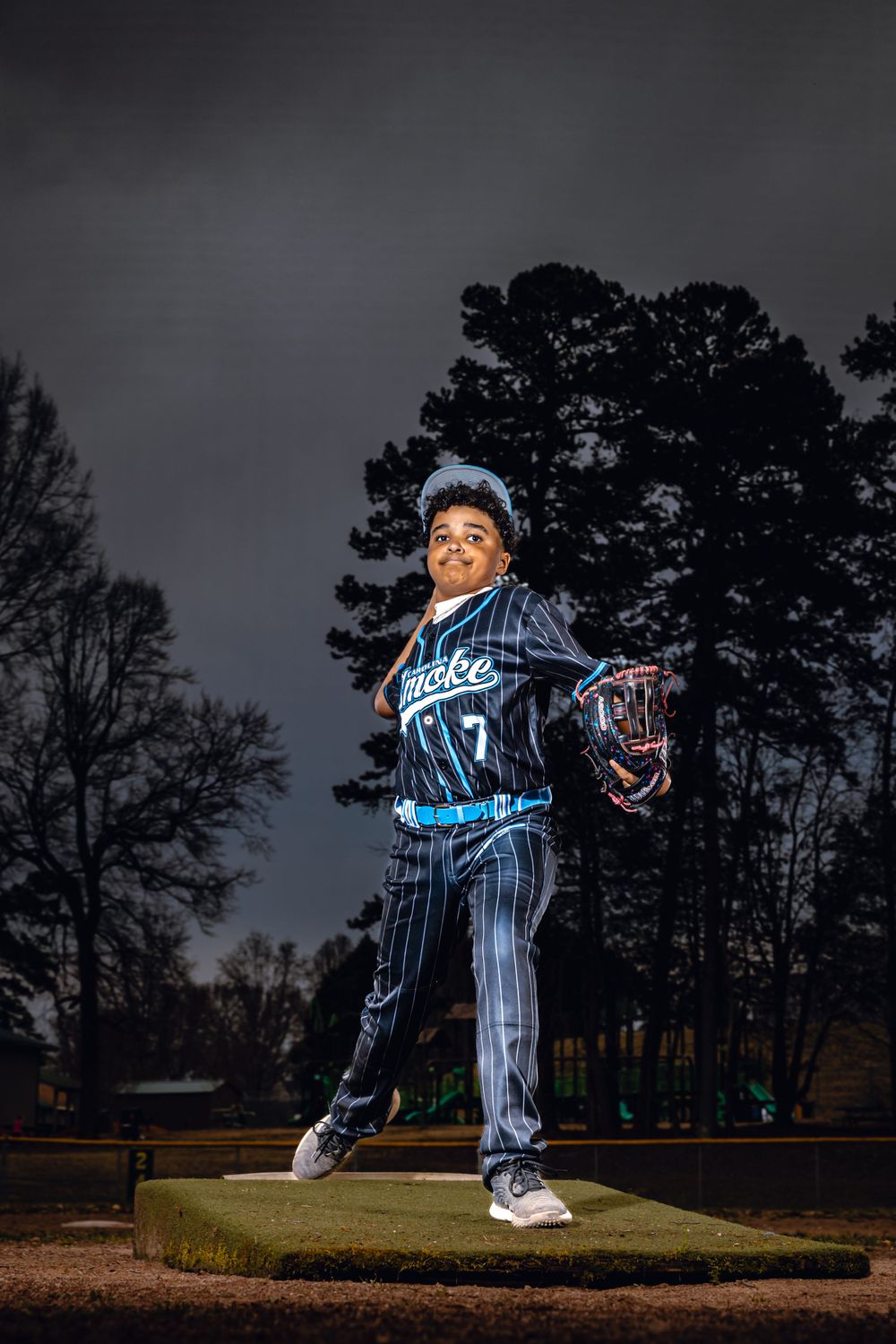 Baseball player practicing pitching motions on a field at dusk.