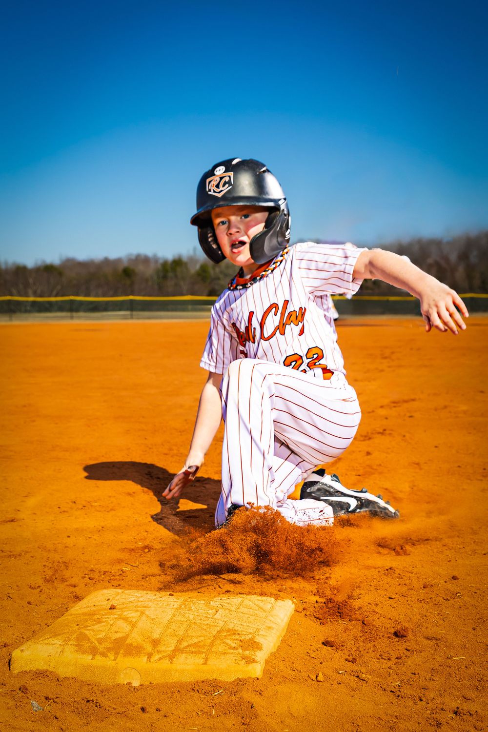 Baseball player sliding into base with dramatic dirt cloud on orange clay field.