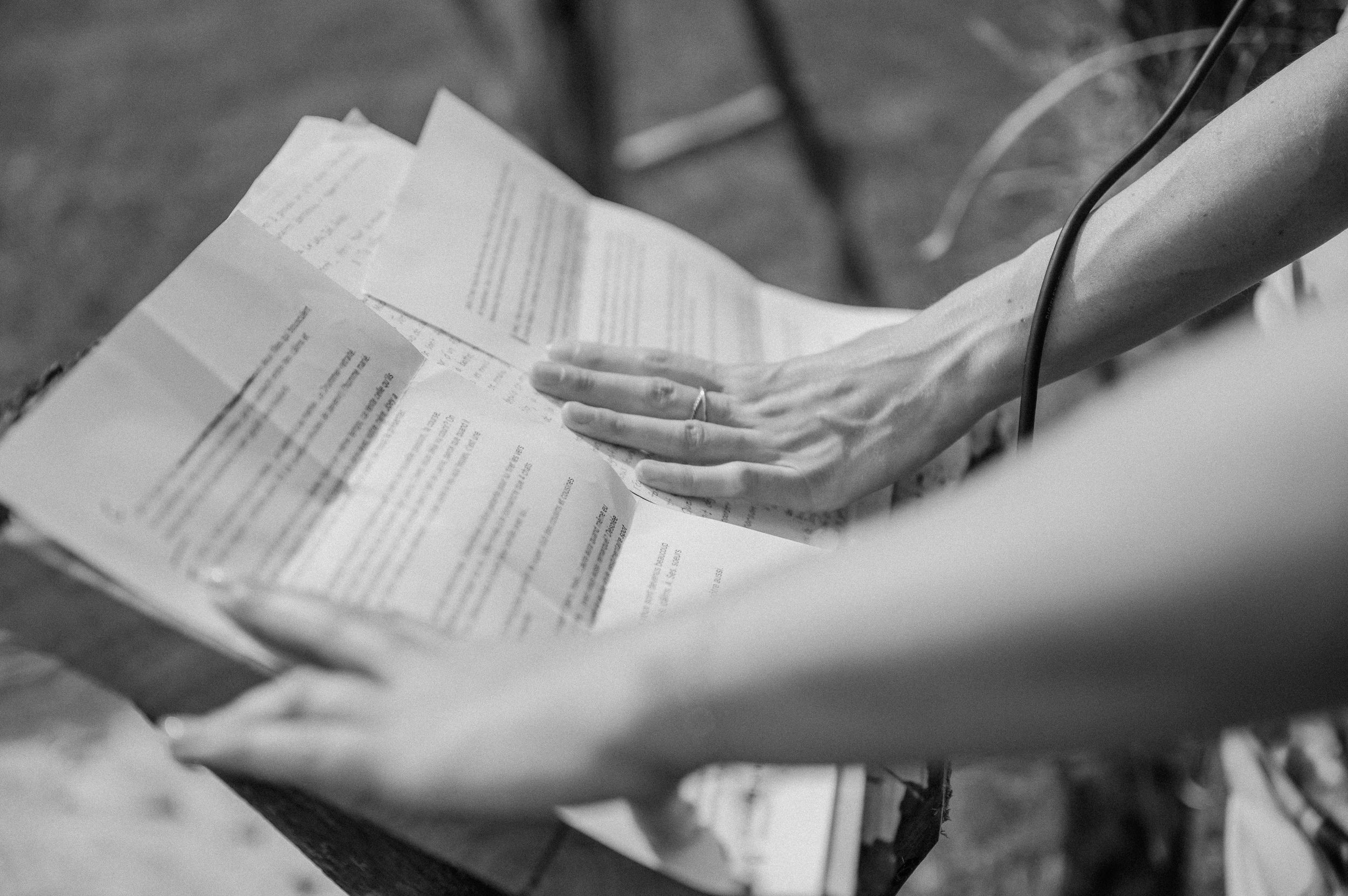 Black and white closeup of hands holding document papers while reading outdoors.