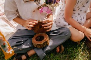 Two people sitting on grass enjoying drinks and snacks at an outdoor summer picnic.