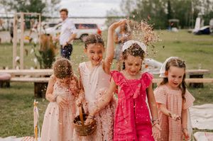 Four girls in pink and coral dresses playfully toss autumn leaves during an outdoor photoshoot.
