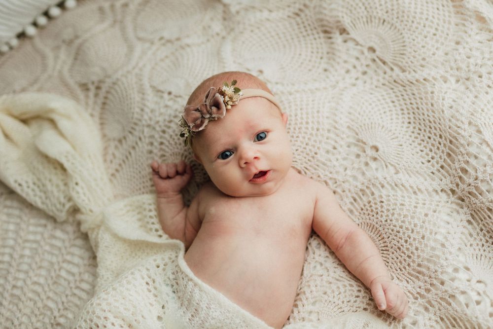 Newborn baby swaddled in white lace blanket during professional photoshoot.