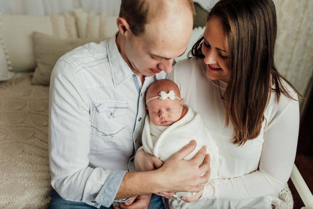 Candid family photoshoot showing parents lovingly embracing their newborn baby.