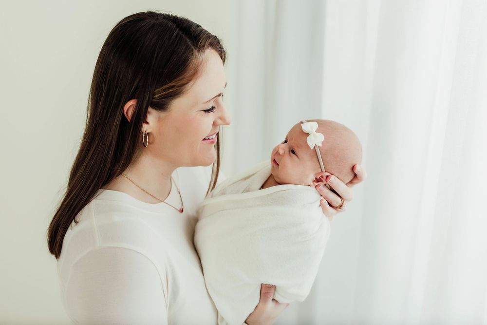 Lifestyle newborn session showing tender moments between mother and baby in soft white tones.