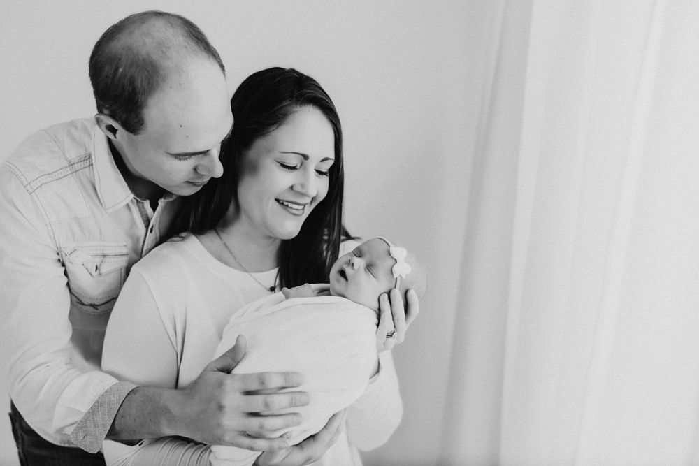 Minimalist family photography session with gentle embraces in white room setting.