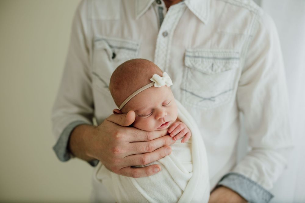 Parent tenderly holding sleeping newborn baby in white buttoned shirt.