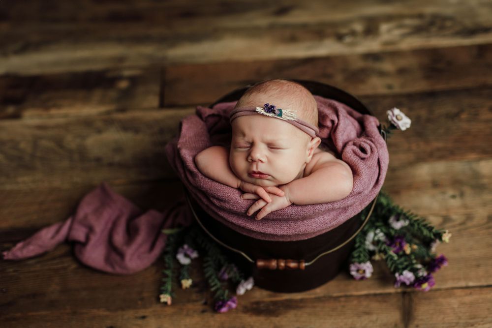 Rustic newborn photography featuring baby nestled in pink fabric with floral elements.