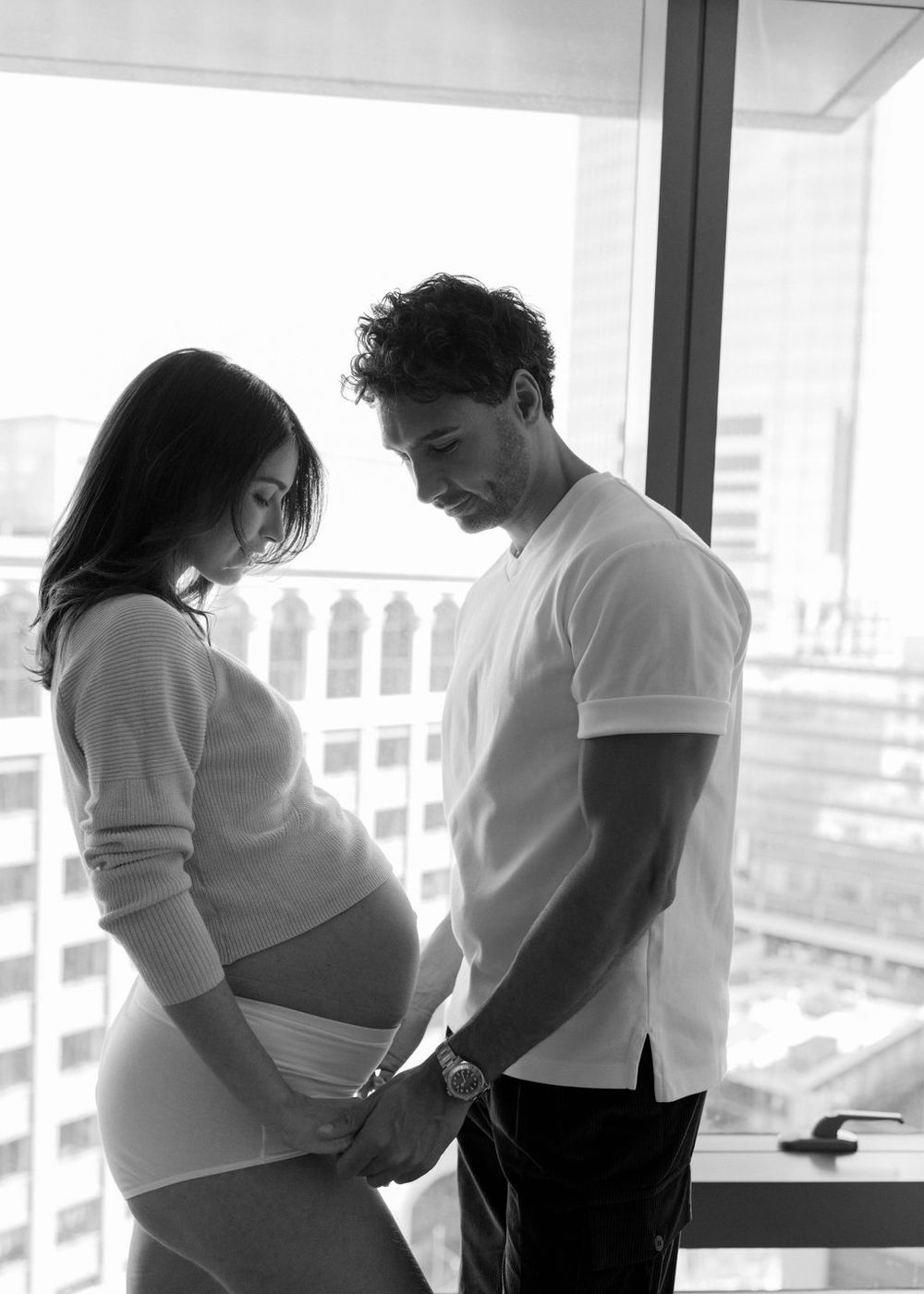 A series of pregnant women stand silhouetted against a bright window in a row during a maternity photoshoot.