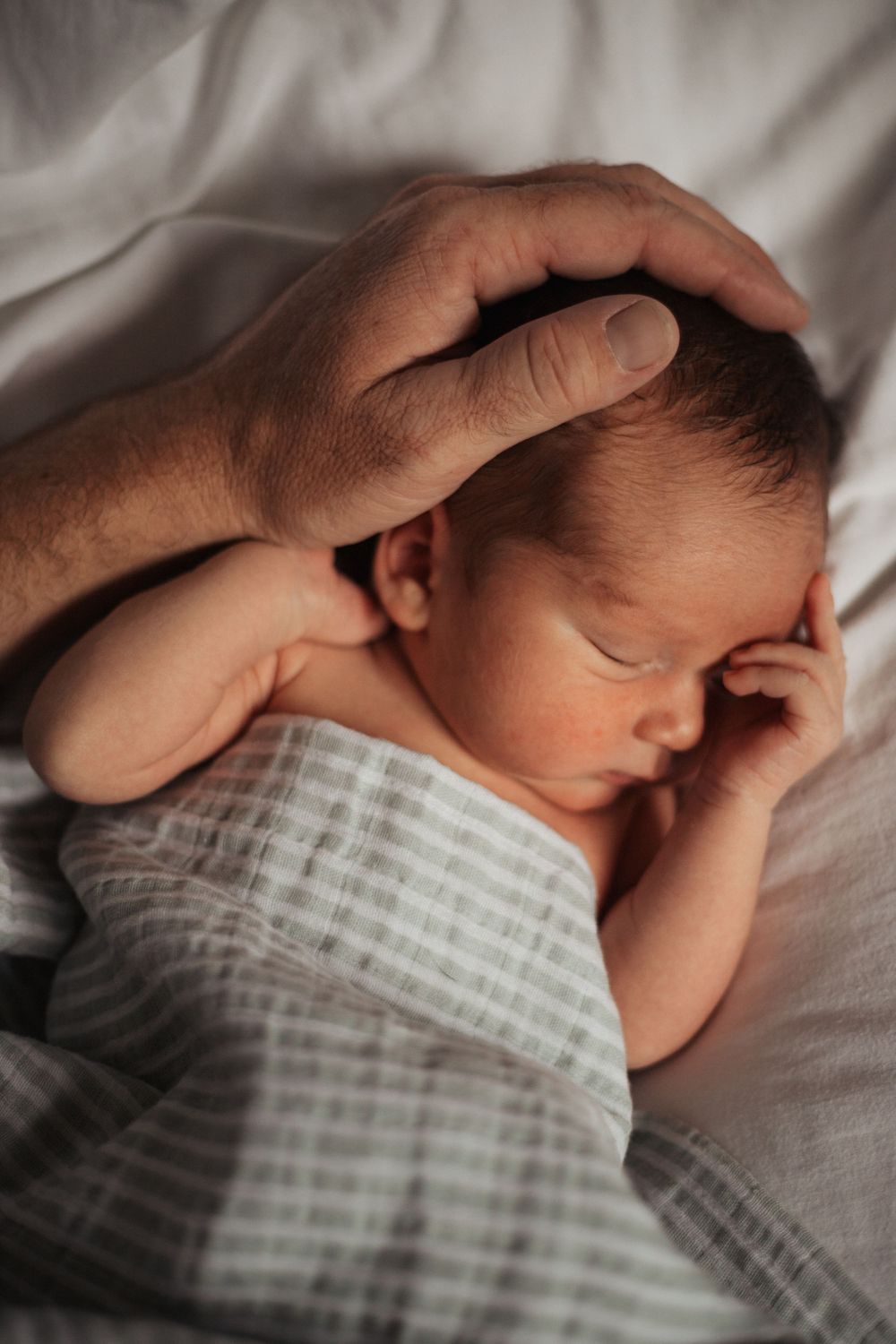 Sleeping newborn wrapped in striped blanket with adult hand gently touching head.