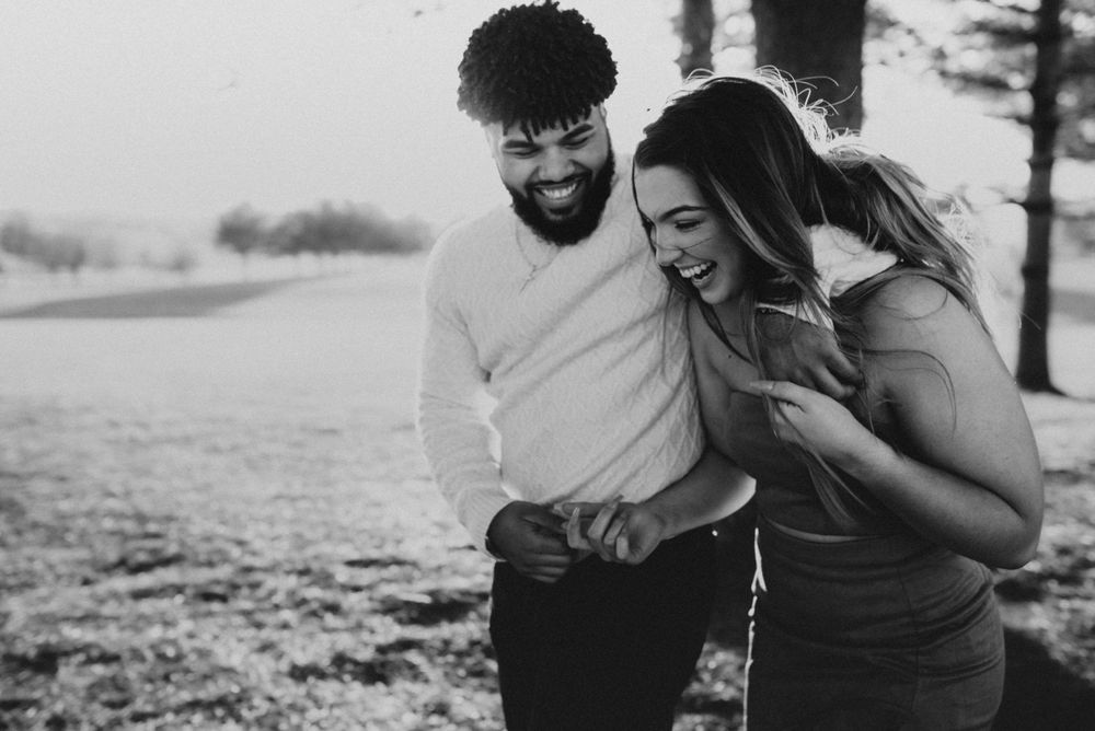 Candid black and white photo of a laughing couple sharing a joyful moment outdoors.