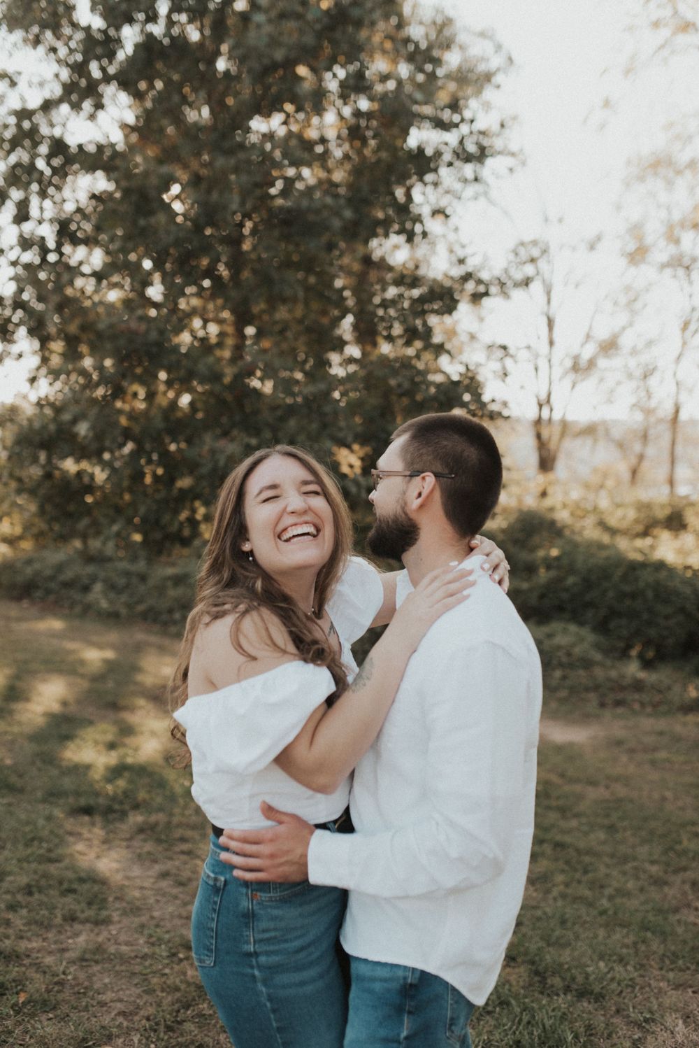 A candid engagement photo showing a couple laughing together in golden sunset light.