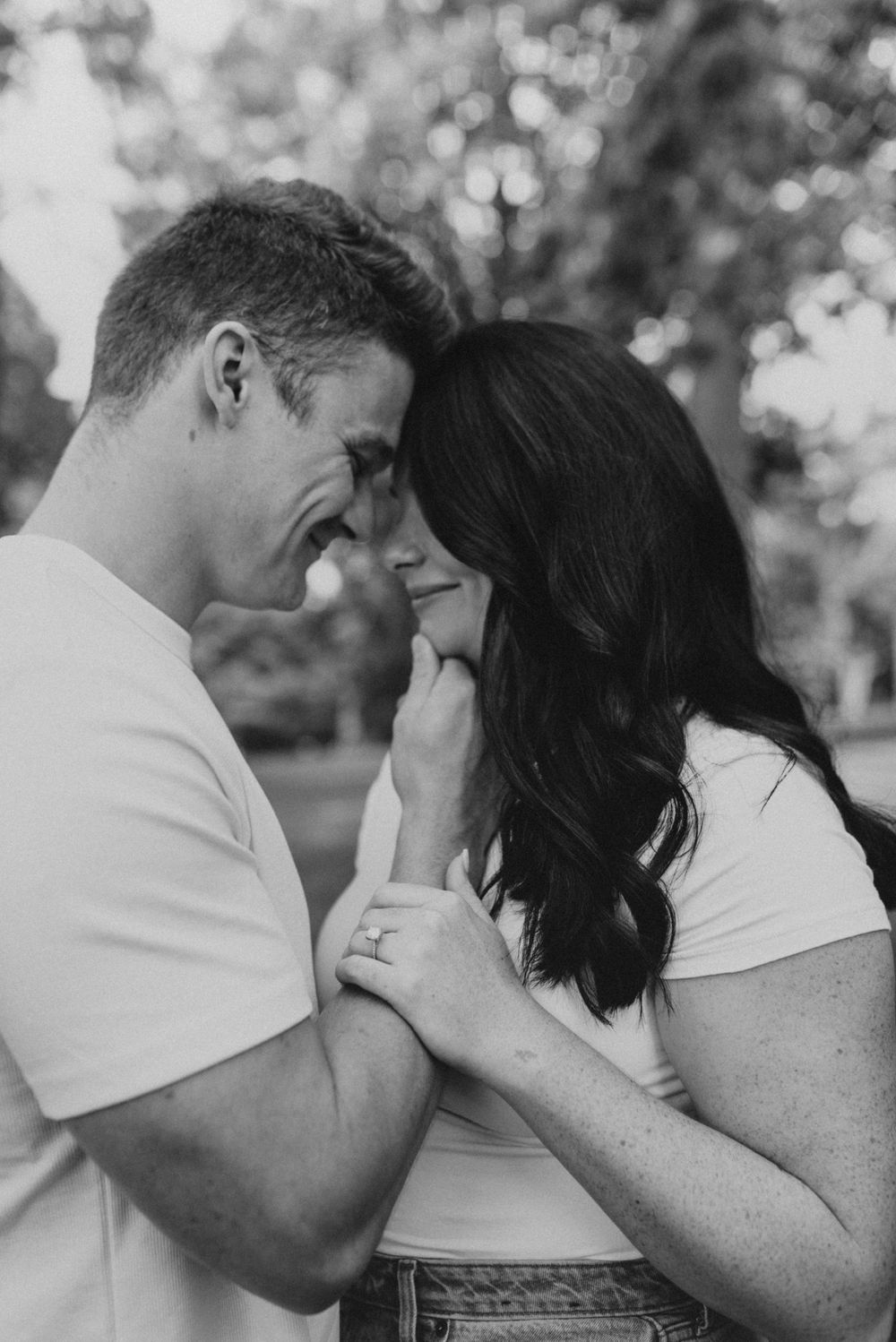 Intimate black and white photo of a couple in white shirts sharing a tender moment outdoors.