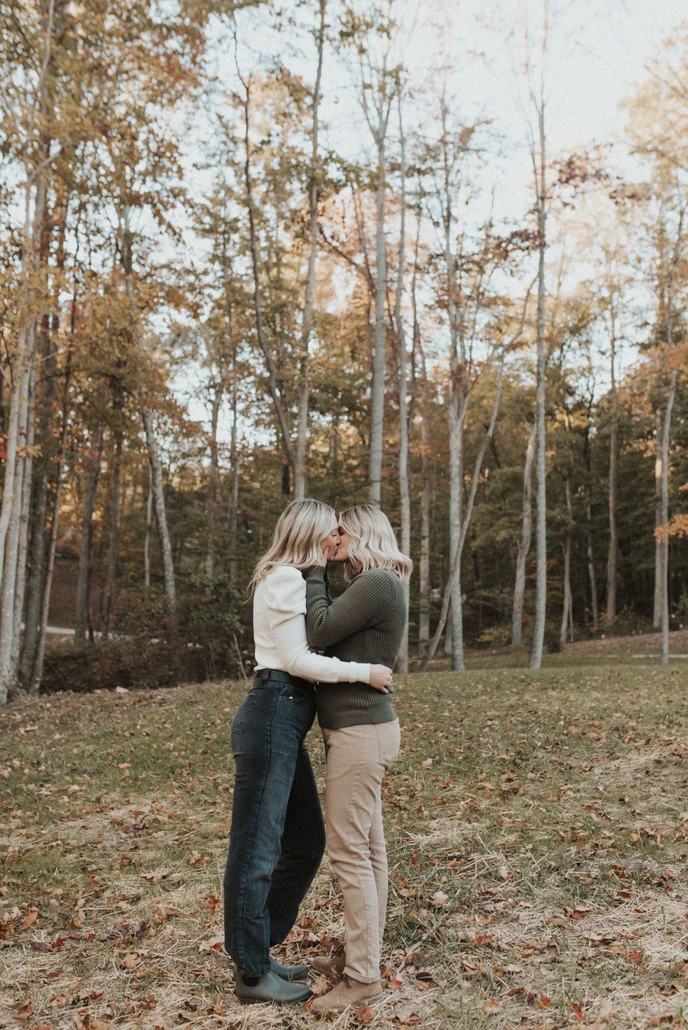 Romantic autumn portrait of embracing couple surrounded by tall trees in forest setting.