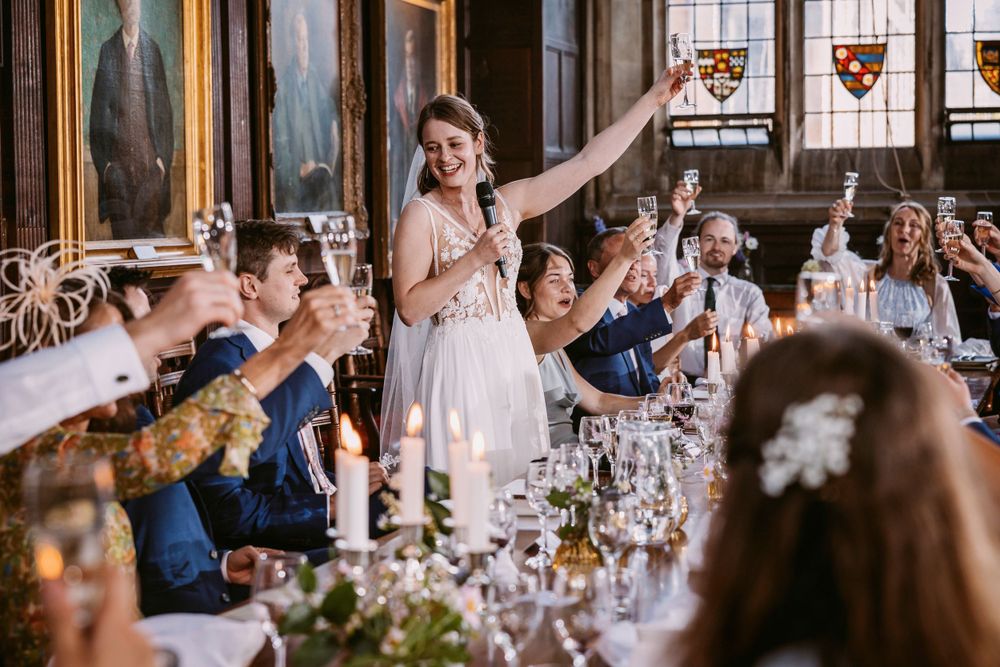Wedding reception scene shows guests celebrating with toasts in an elegant dining hall at Balliol College, Oxford