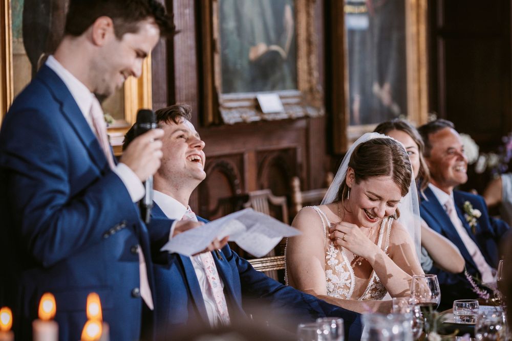 Balliol College, Oxford wedding. Emotional reactions during wedding speeches in a grand hall with candlelit tables and ornate decor.