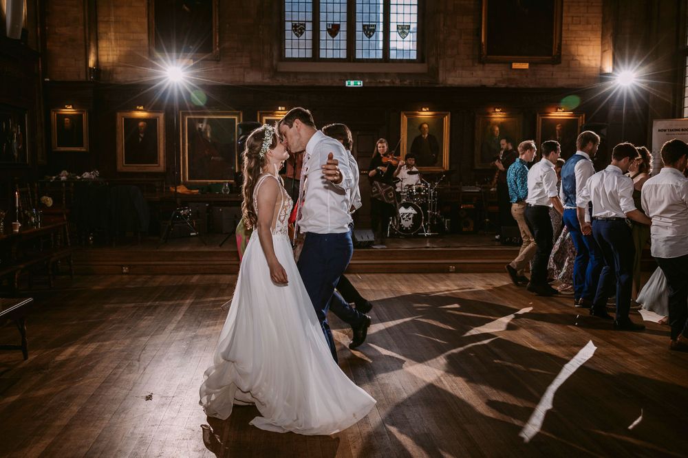 Wedding couple shares a romantic dance moment in a grand hall with dramatic spotlighting at Balliol College, Oxford