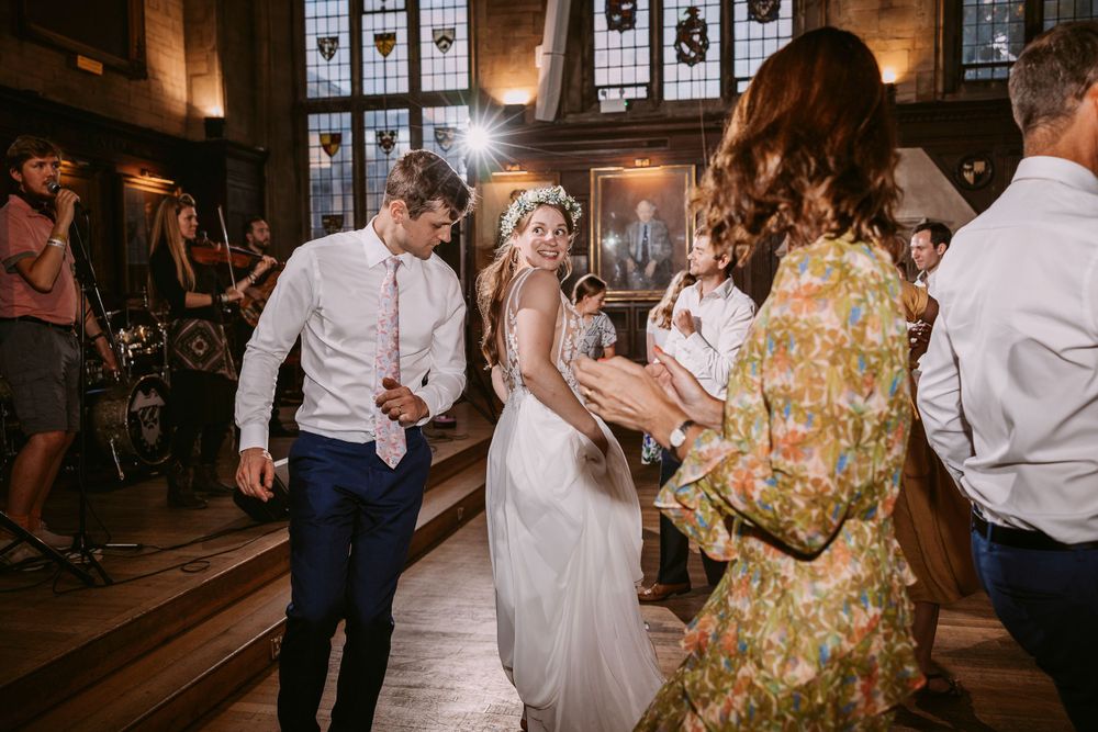 Energetic ceilidh dancing at wedding reception in historic venue with stained glass windows and wooden floors at Balliol College, Oxford