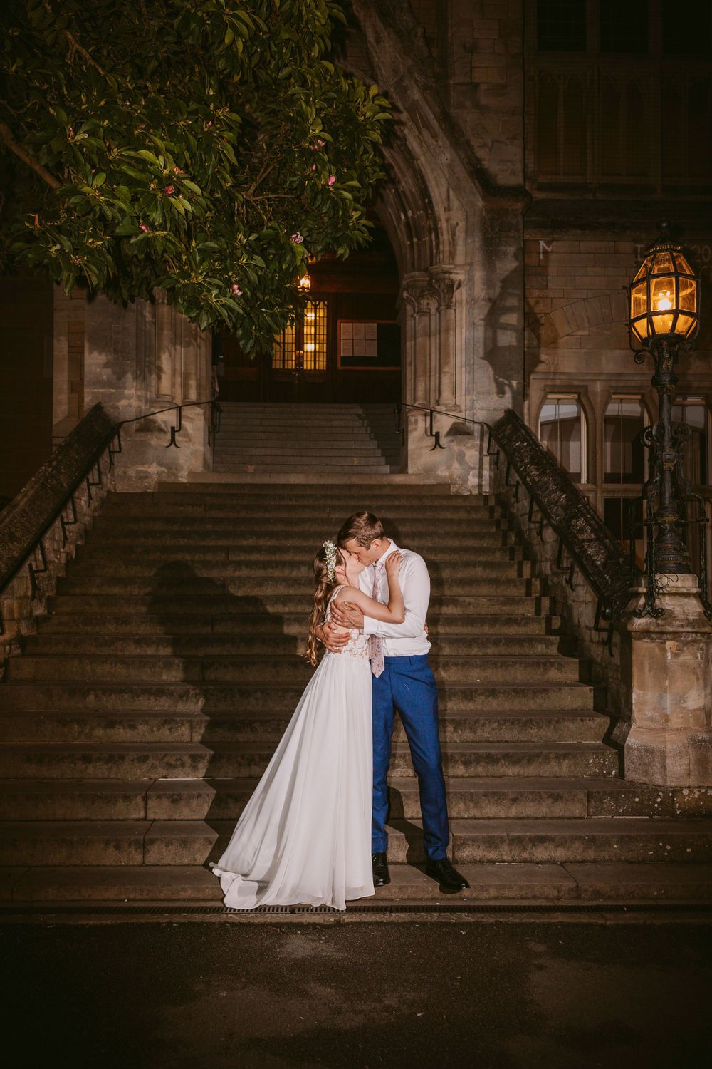 Romantic nighttime portrait of newlyweds on stone steps with gothic architecture and lantern lighting at Balliol College, Oxford