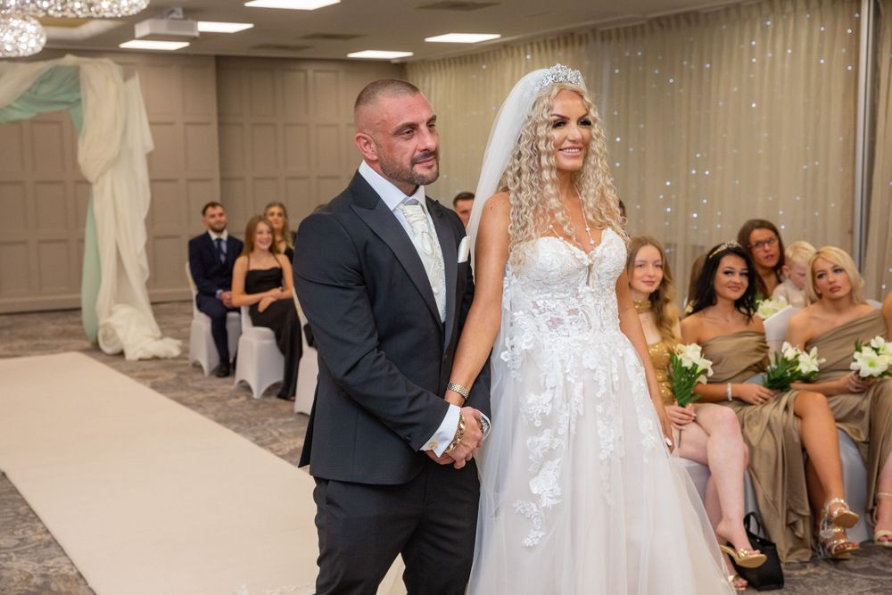 Bride in lace gown and groom in navy suit walk down the aisle hand in hand.