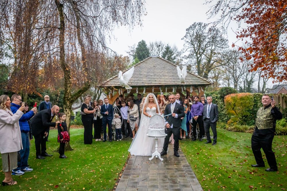 Bride and groom walk down outdoor path as wedding guests line up to celebrate in an autumn garden setting.