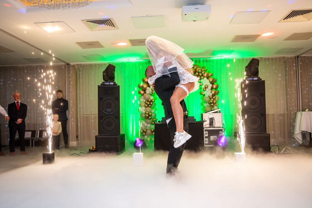 Groom lifts bride during dramatic first dance with sparkling pyrotechnics and green lighting on dance floor.