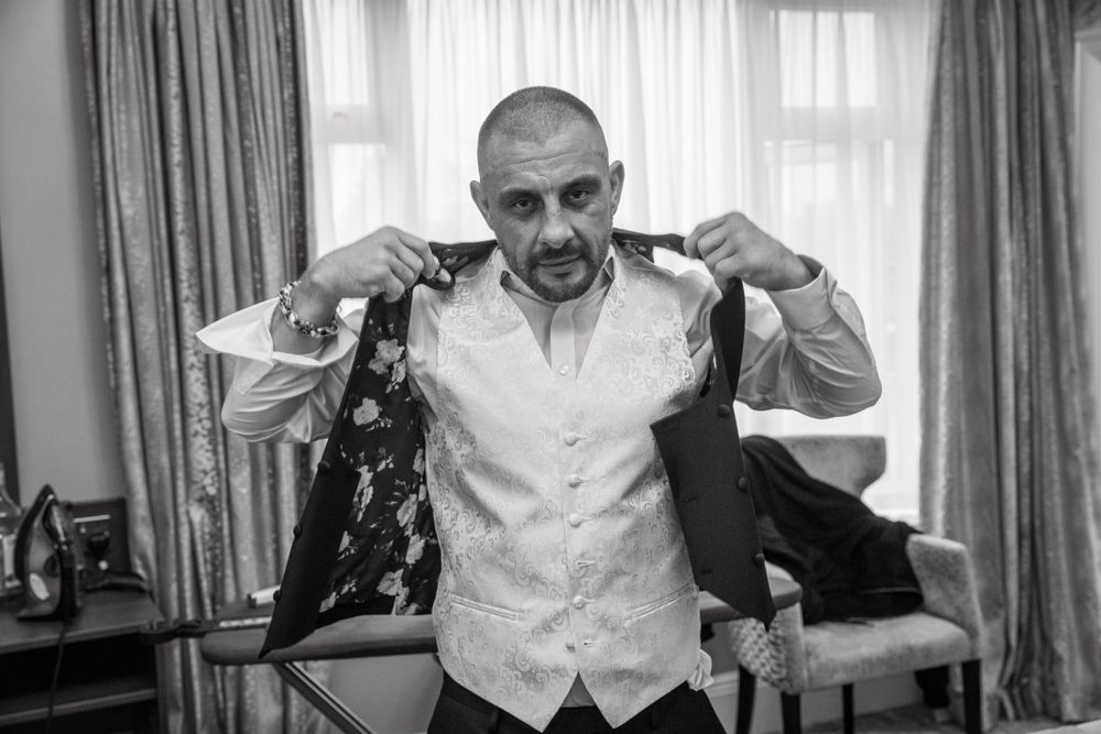 Groom adjusting his waistcoat while getting ready for his wedding day in black and white.
