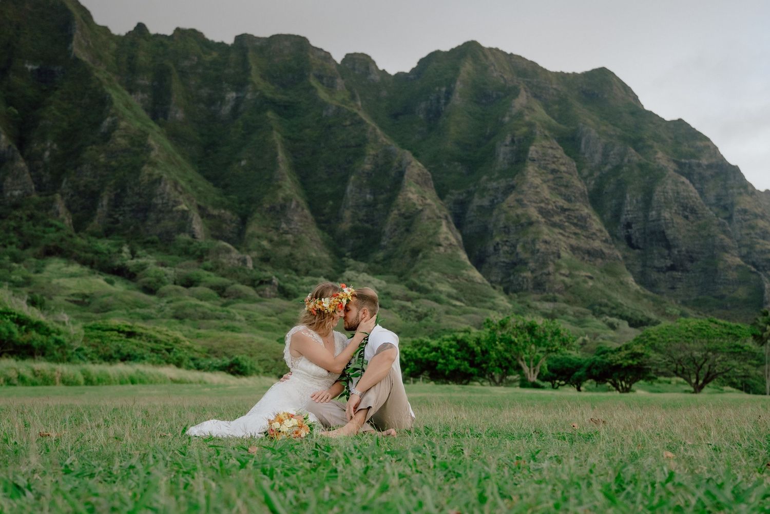 A couple shares a romantic moment in front of lush green mountains of Kualoa Ranch in Hawaii.