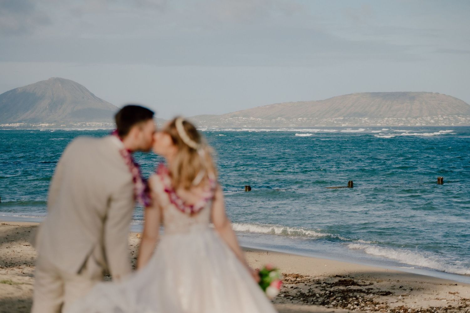 A beachside wedding ceremony with guests seated on chairs overlooking the ocean as waves roll onto the shore.