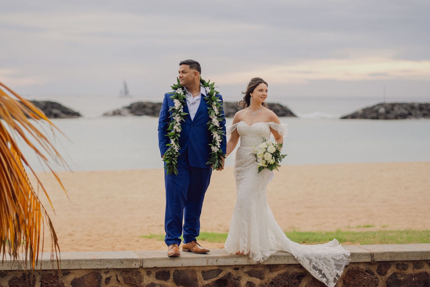 Couple in wedding attire walking along a scenic beach at Magic island oahu hawaii in sunset