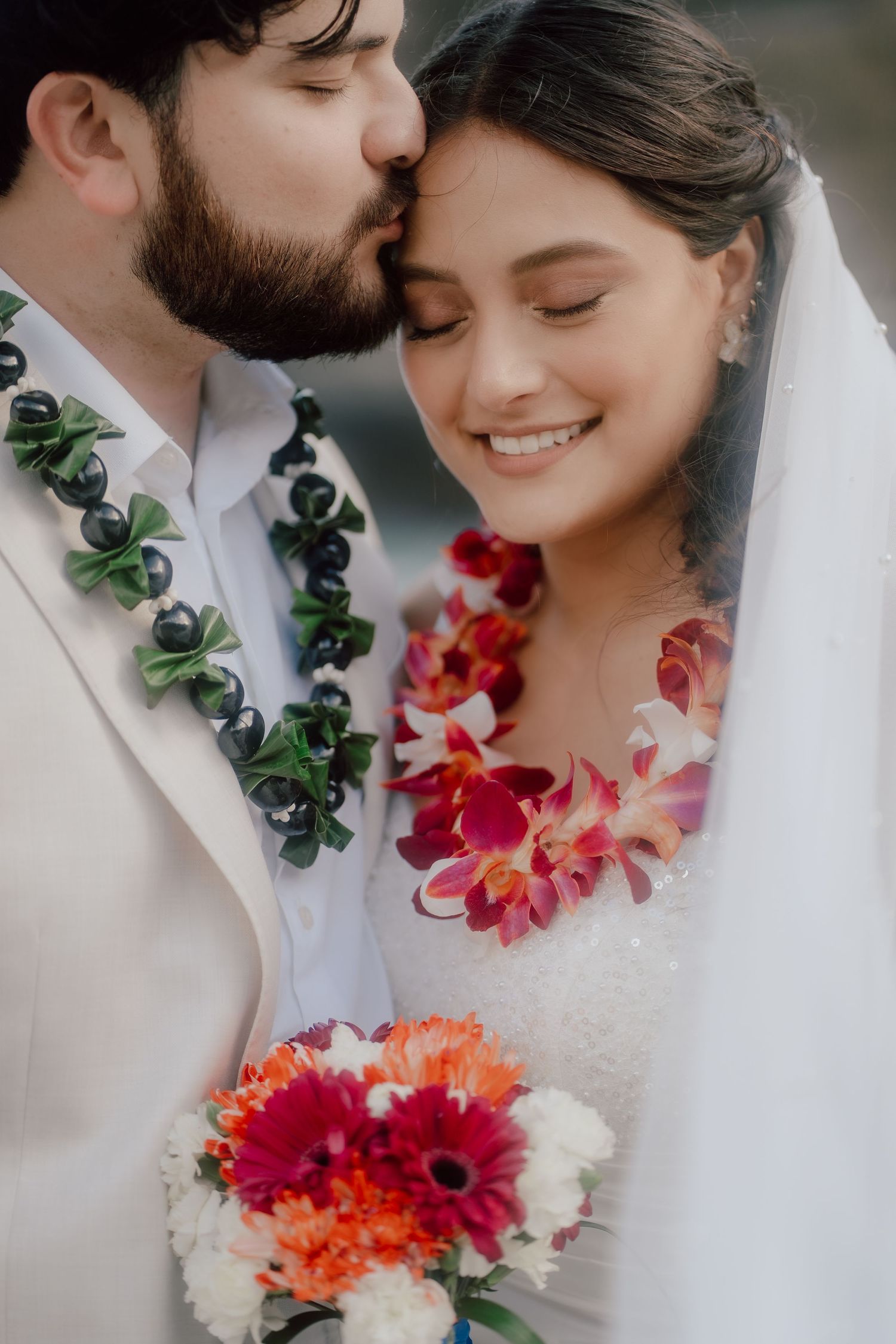 Romantic wedding portrait showing couple wearing traditional Hawaiian leis with bright tropical flowers and bridal bouquet.