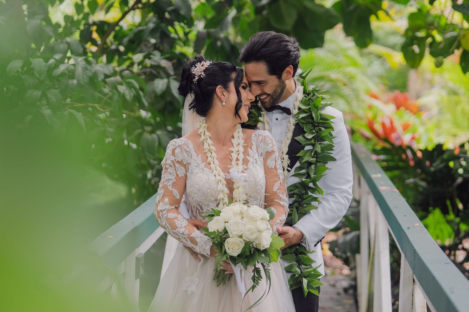 A romantic wedding couple embraces in a lush garden setting with white floral decorations and natural greenery.