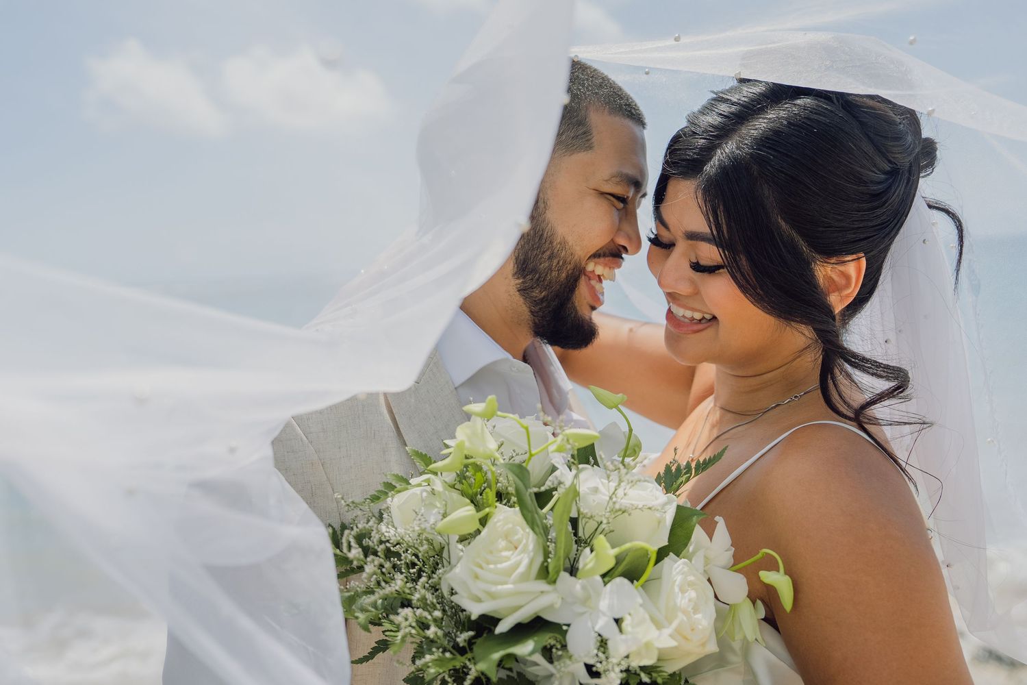 joyful wedding couple shares an intimate moment under a flowing veil holding a white and green floral bouquet coordinator Wedding of Hawaii