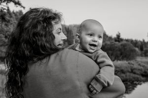 A joyful baby in a sweater laughs while being held outdoors in this black and white portrait.