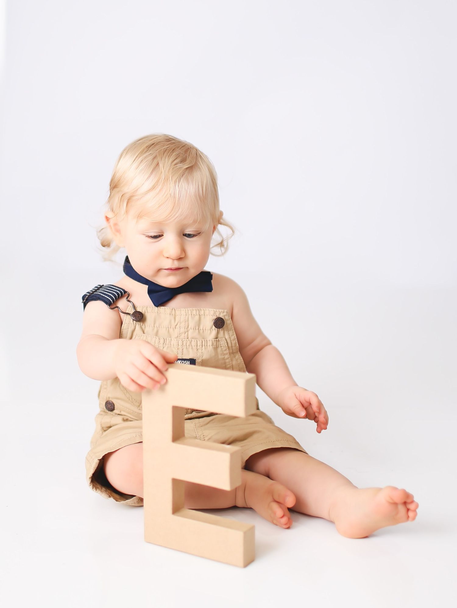Baby boy holding cardboard letters to spell ONE for cake smash session
